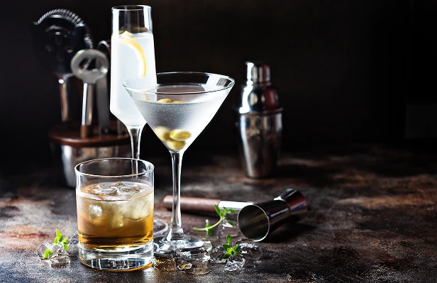 An elegant cocktail arrangement featuring a martini glass and a rocks glass alongside a metal shaker and jigger on a dark textured surface.