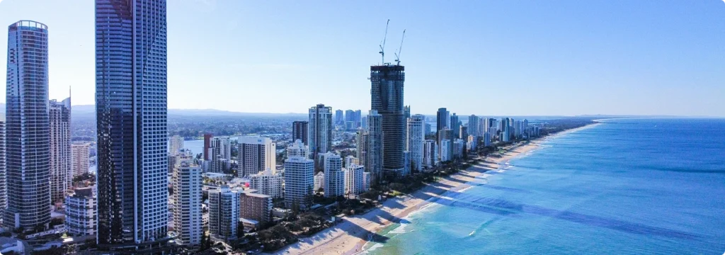 An aerial panoramic view of the Gold Coast skyline with high-rise buildings lining a long sandy beach along turquoise ocean waters.