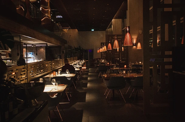 A dimly lit Kerlinka dining room with warm pendant lighting and set tables, ready for evening guests.
