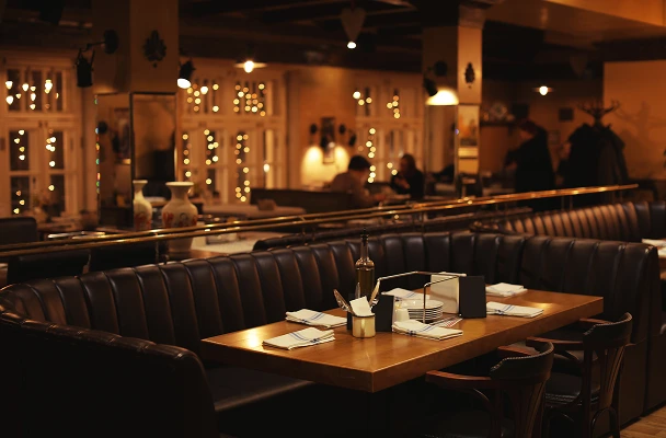 A cozy, well-lit restaurant dining room with dark walls, wooden decorative elements, pendant lights, and tables